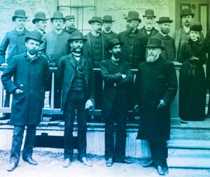 fifteen men and two women stand outside a building entrance circa 1895
